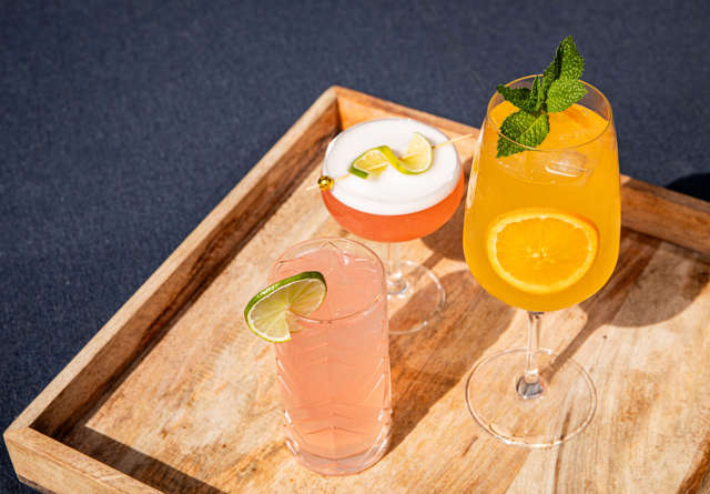 Wooden tray with summer cocktails decorated with fresh garnishes.