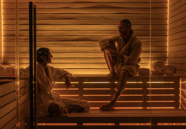 Two people relaxing in a sauna, wearing robes, illuminated by warm lighting for a serene atmosphere.
